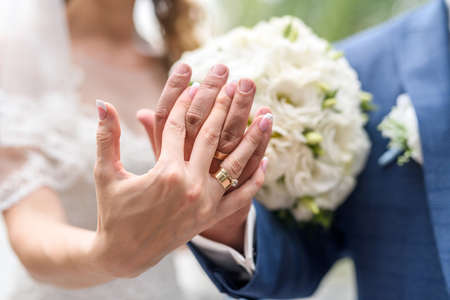 Wedding concept. Male and female hand with golden rings on flower bouquetの写真素材