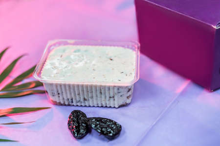 Delicious dessert in plastic package with prunes on table and violet wrapping close up. Food concept
