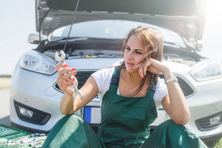 Beautiful woman in overalls with the keys repairing a broken car in her journey