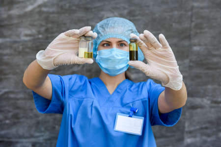 Medical worker in blue uniform holding ampoules with vaccines of different color on abstract...