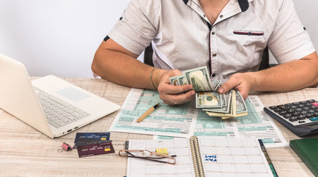 Businessman fills in tax form 1040 with laptop and calculatorの写真素材