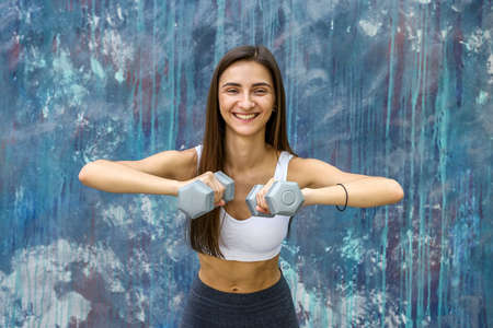 Woman doing fitness exercises. Young woman with dumbells posing outdoors
