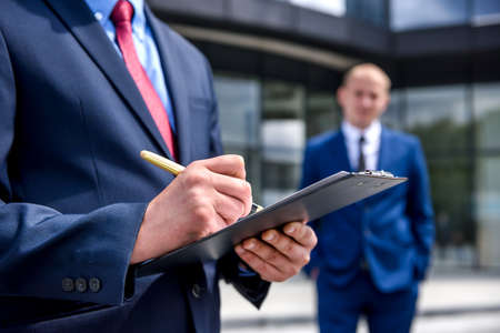 Man in suit with clipboard standing outdoorsの写真素材