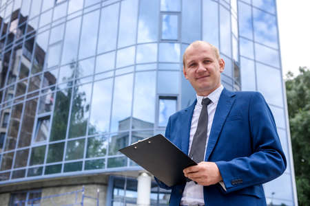 Businessman with clipboard standing against new buildingの写真素材
