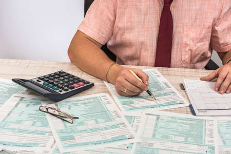 Man filling 1040 tax form at workplace. Performing tax calculations. Close up