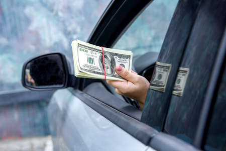 Bribe concept. Female hands giving dollar bundle inside car close up