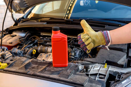 Oil change concept. Male hand in glove with oil bottle and car engine close upの写真素材