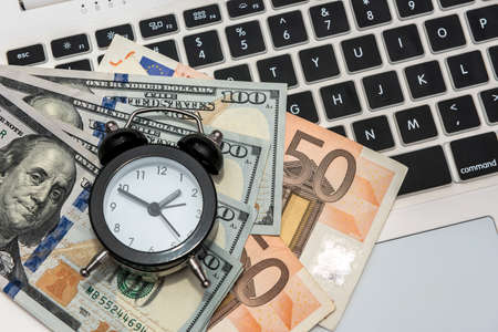 Business concept - laptop money dollars and euro with clockの写真素材