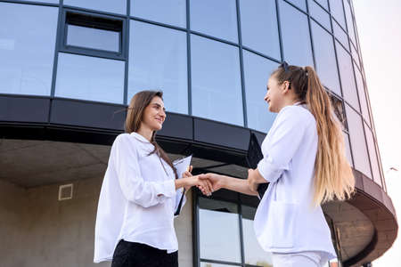 Partnership. Two young business ladies handshaking outside office building