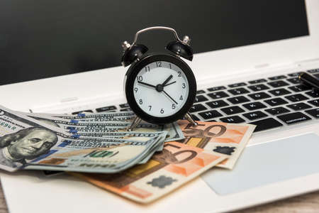 Business concept - laptop money dollars and euro with clockの写真素材