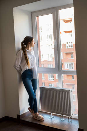 Portrait of elegant european woman in casual clothes looking out of window and enjoying sunny weatherの写真素材