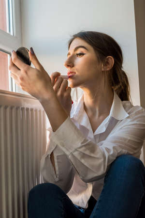 girl doing itself makeup near window in the background before taking a photossesion