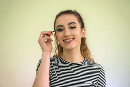 Beautiful girl paints eyelashes morning before work isolated on green.