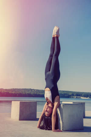 Young brunette woman in sportswear doing stretching her legs after the workout on the lake near...