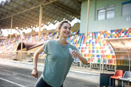 Young and sportive woman holding bottle of water. She's doing morning exercises on open air