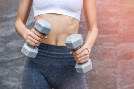 Happy young woman with dumbbells making exercises outdoors in front of modern painted wallの写真素材