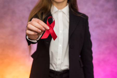 AIDS concept. Woman holding red ribbon in hands close up