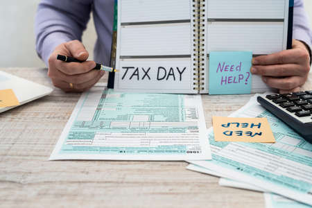 A man in a business suit writes a 1040 tax form in the office. Male hands fill on paper with calculator at workplace. Accounting conceptの写真素材