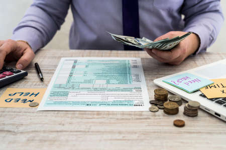 businessman counts dollars and fills out a US 1040 individual tax form. Sticker with the inscription tax time. Tax concept.の写真素材