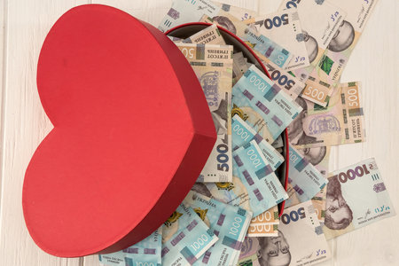 A red heart-shaped box full of money. UAH Money of Ukraine 1000 and 500 banknotes on deskvの写真素材
