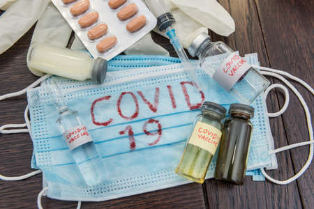 Coronavirus as danger disease. COVID-19 write on blue medical face mask and virus vaccine ampoule....