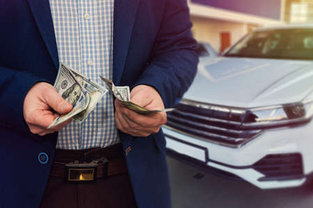 salesman selling auto in car shop or businessman buying new car holding dollar in hand.