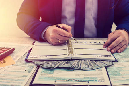 A businessman fills out an individual 1040 tax form and counts dollars. Male hands writing on paper...