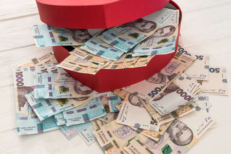 A red heart-shaped box full of money. UAH Money of Ukraine 1000 and 500 banknotes on deskv