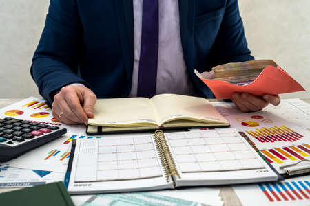 Businessman receives hidden income in an envelope from the company. A man works with a business schedule and keeps a profit in the office. The concept of pay or corruption.の写真素材