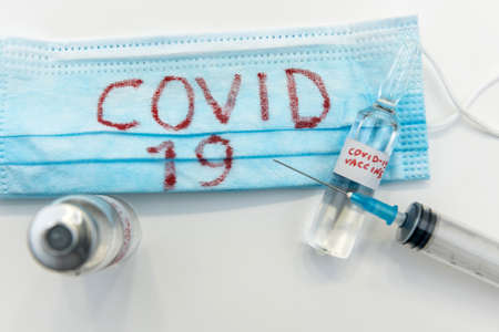 coronavirus epidemic concept. medical face mask with a red inscription COVID-19 and syringe with possible found vaccine. pandemic.の写真素材