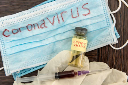 COVID-19 coronavirus ampoule with a vaccine, infected blood in the syringe, medical mask. Dangerous diseases and viruses.の写真素材