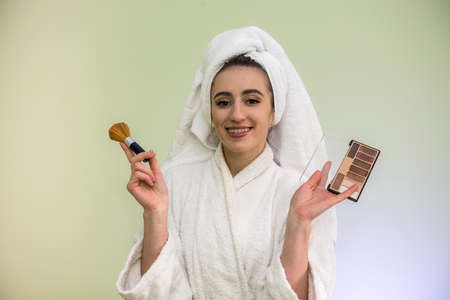 beautiful young woman in a bathrobe and towel after shower is doing herself a makeover - apply powder on face.の写真素材