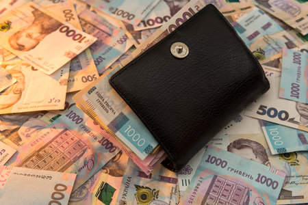 The thick money-laden black men's wallet lies against the backdrop of Ukrainian hryvnia money. Concept of saving moneyの写真素材