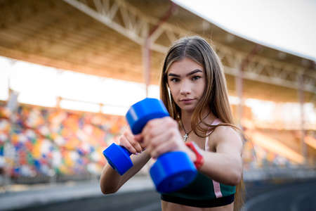 Young fitness woman working out with dumbbells in the city stadium. Sports conceptの写真素材
