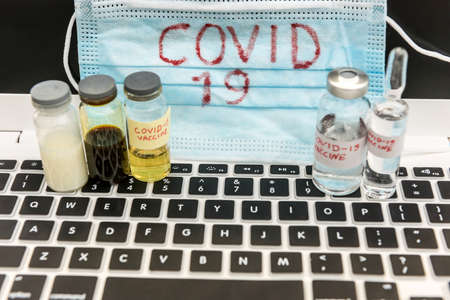 2019 Coronavirus write on vedical mask with vaccine in ampoule and laptop. Worldwide epidemic. Virus vaccine search conceptの写真素材
