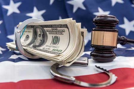Metal handcuffs, judge's hammer and dollar bills lying on flag of American. financial crime or corruption conceptの写真素材