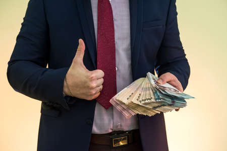 A man in a suit holds a large pile of Ukrainian money and shows his income. UAH. new banknotes 1000 and 500 hryvniaの写真素材