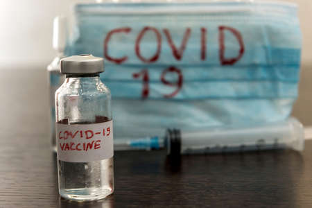 COVID-19 coronavirus ampoule with a vaccine, infected blood in the syringe, medical mask. Dangerous diseases and viruses.の写真素材