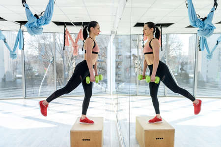 Athletic woman pumping up muscles with dumbbells before workday at fitness gym. health lifestyleの写真素材