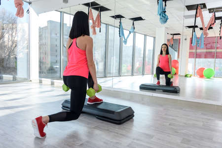 Young and sportive woman exercising in gym with dumbells