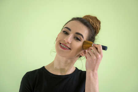Attractive girl with makeup brushes isolated on green. concept of beauty and health