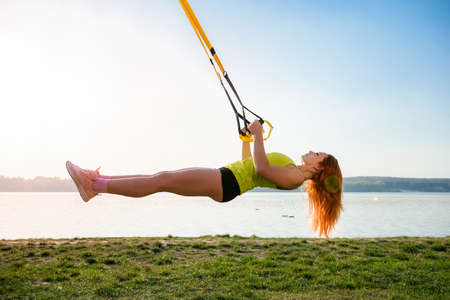 young female athlete doing morning exercises training with fitness straps in the park. Concept of healthy workout and lifestyleの写真素材