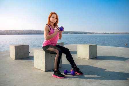 young beautiful girl is engaged in morning gymnastics with dumbbells at the lake