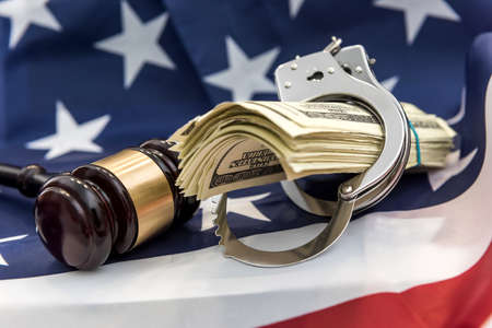 Metal handcuffs, judge's hammer and dollar bills lying on flag of American. financial crime or corruption conceptの写真素材