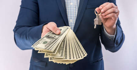 Male hands holding US dollars bills and house key isolated. Concept buy or real estate loanの写真素材