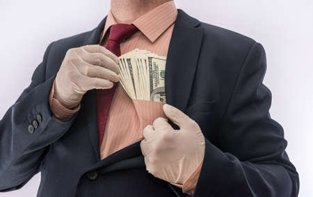 Man in suit holding money dollars 100 bills in medical gloves for safety. Coronavirus crisis. covid-19の写真素材