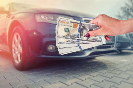 salesman selling auto in car shop or businessman buying new car holding dollar in hand.の写真素材