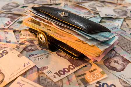The thick money-laden black men's wallet lies against the backdrop of Ukrainian hryvnia money. Concept of saving moneyの写真素材