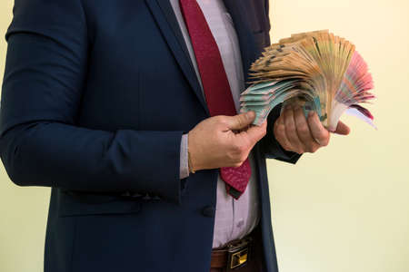 A man in a suit holds a large pile of Ukrainian money and shows his income. UAH. new banknotes 1000 and 500 hryvniaの写真素材
