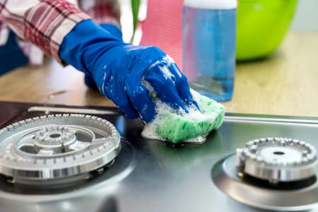 Woman cleaning stainless steel gas surface in the kitchen with rubber gloves.の写真素材